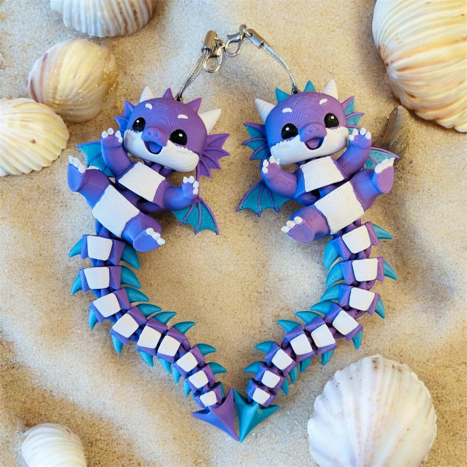 Articulated 3D printed baby dragon and raccoon keychain fidget toys on patterned fabric