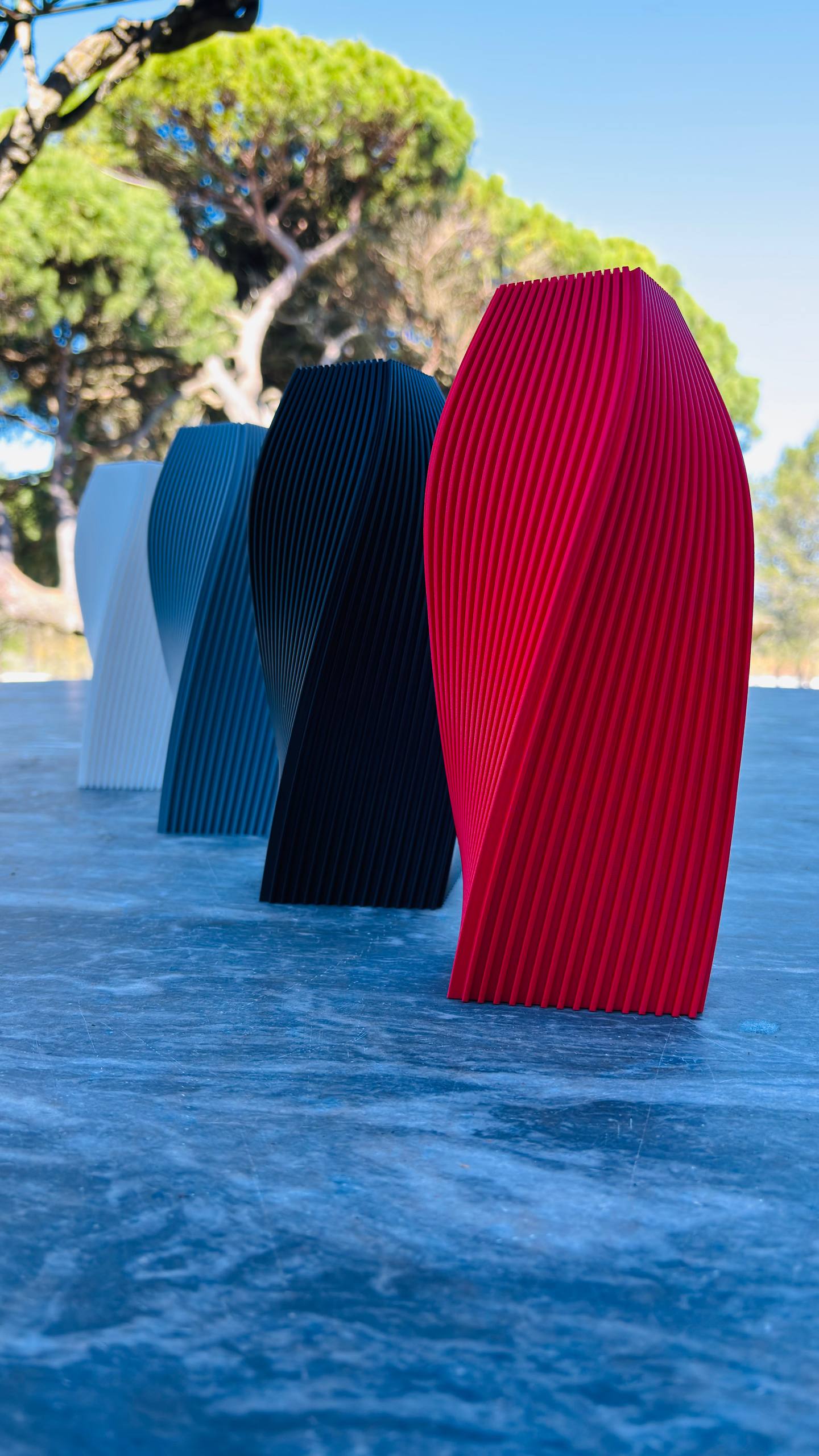 A row of colorful 3D printed Helixa vases with a parametric twisted design shown outdoors.